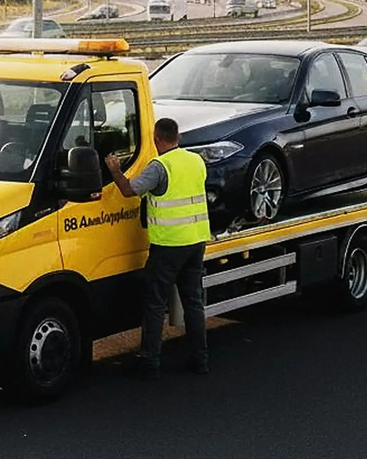 Mitarbeiter in Warnweste sichert ein Auto auf dem Abschleppwagen